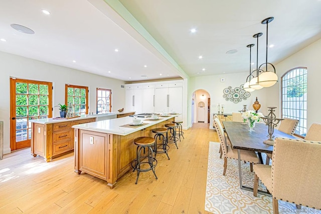 kitchen with hanging light fixtures, light hardwood / wood-style floors, a kitchen island, a kitchen bar, and kitchen peninsula