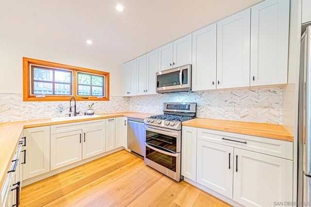 kitchen with white cabinets, butcher block counters, stainless steel appliances, and light hardwood / wood-style flooring