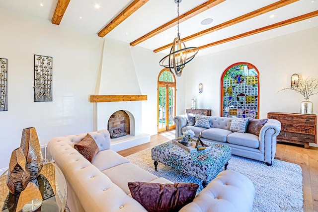 living room featuring a chandelier, beam ceiling, light hardwood / wood-style floors, and a fireplace