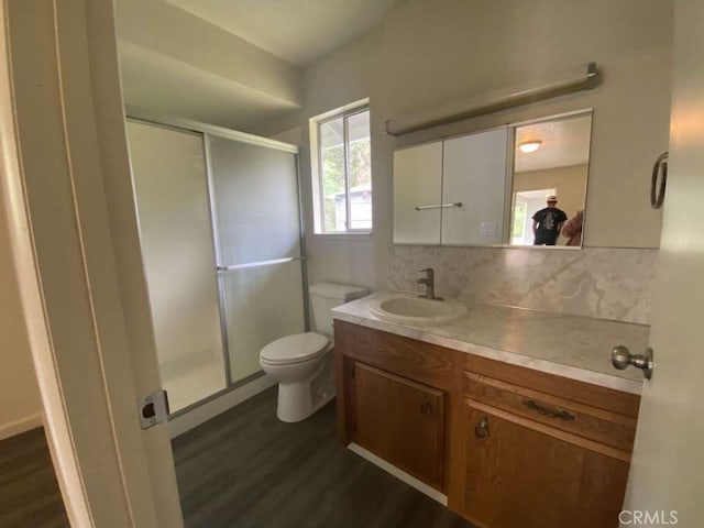 bathroom with wood-type flooring, backsplash, walk in shower, vanity, and toilet