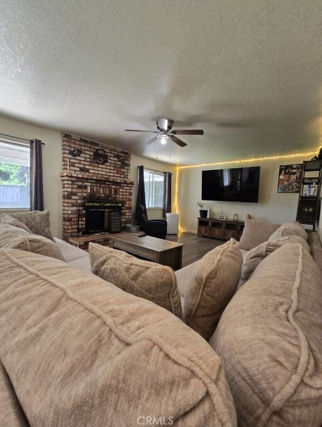 living room featuring a textured ceiling, ceiling fan, and a brick fireplace