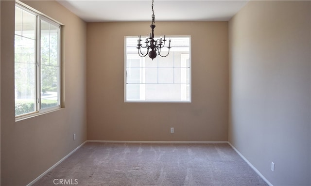 carpeted empty room featuring plenty of natural light and a chandelier