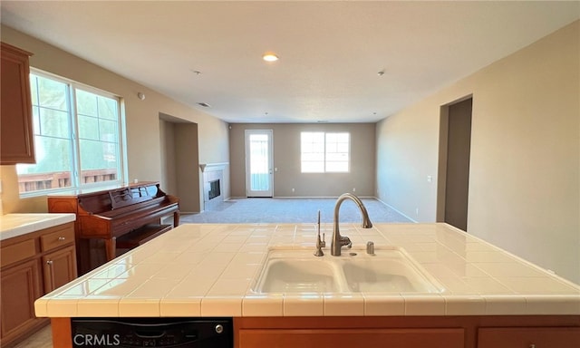 kitchen featuring light colored carpet, tile countertops, a kitchen island with sink, and sink