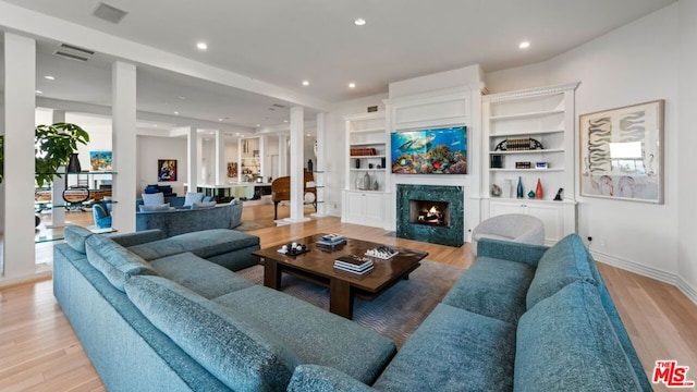 living room with built in features, a high end fireplace, and light hardwood / wood-style floors