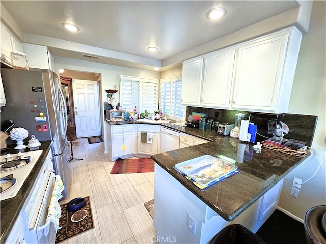 kitchen with white cabinetry, kitchen peninsula, decorative backsplash, white appliances, and dark stone countertops