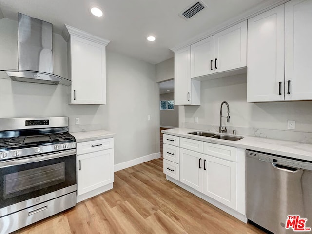 kitchen with white cabinets, wall chimney range hood, sink, light hardwood / wood-style flooring, and stainless steel appliances