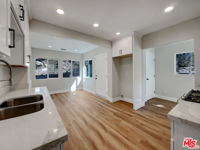 kitchen with light stone countertops, sink, white cabinets, and light hardwood / wood-style floors