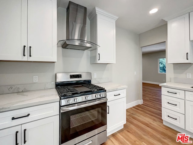 kitchen featuring light stone counters, wall chimney exhaust hood, gas range, light hardwood / wood-style floors, and white cabinetry