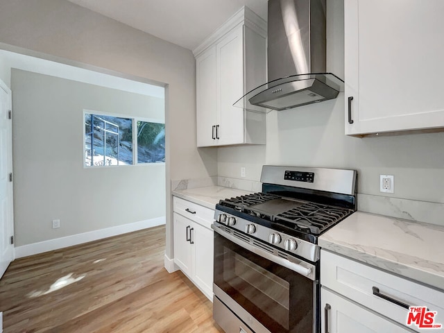 kitchen with gas range, wall chimney exhaust hood, light stone counters, white cabinets, and light wood-type flooring