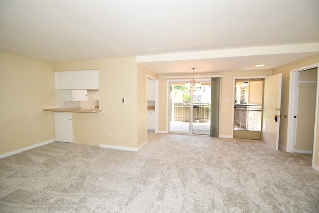 unfurnished living room featuring an inviting chandelier and light carpet