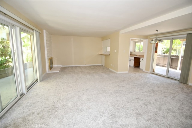 unfurnished living room with light carpet, an inviting chandelier, a fireplace, and plenty of natural light