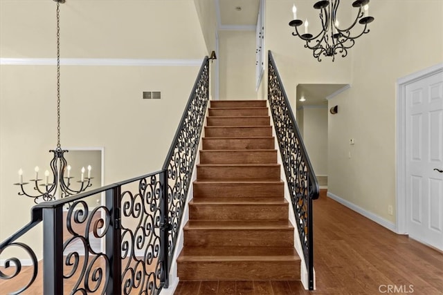 staircase featuring hardwood / wood-style flooring, crown molding, and a notable chandelier