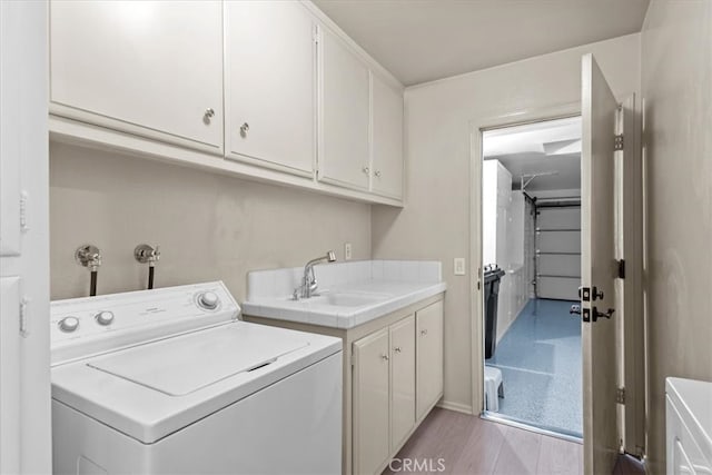 clothes washing area featuring washer / clothes dryer, sink, light hardwood / wood-style flooring, and cabinets