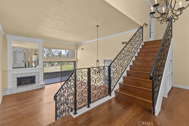 staircase featuring an inviting chandelier, a tiled fireplace, hardwood / wood-style flooring, and ornamental molding