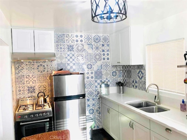 kitchen featuring appliances with stainless steel finishes, white cabinets, wall chimney exhaust hood, sink, and a notable chandelier