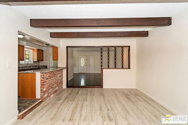 unfurnished living room featuring light wood-type flooring, a textured ceiling, beamed ceiling, and sink