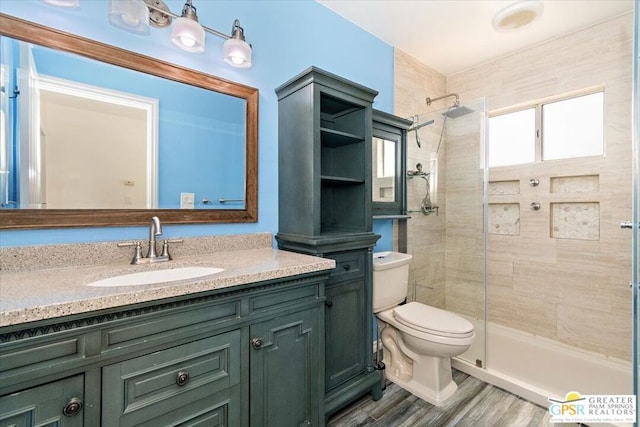 bathroom with hardwood / wood-style floors, a tile shower, vanity, and toilet