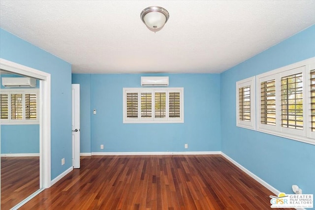 unfurnished bedroom with a textured ceiling, an AC wall unit, dark hardwood / wood-style flooring, and a closet