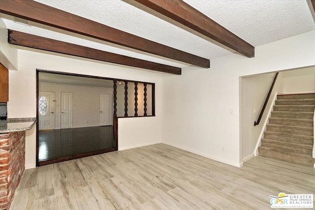 interior space with light hardwood / wood-style floors, beamed ceiling, and a textured ceiling