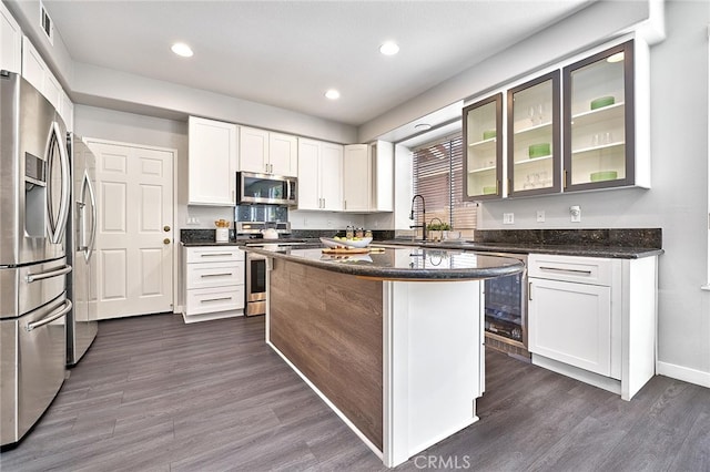 kitchen with appliances with stainless steel finishes, white cabinetry, a center island, and dark hardwood / wood-style floors