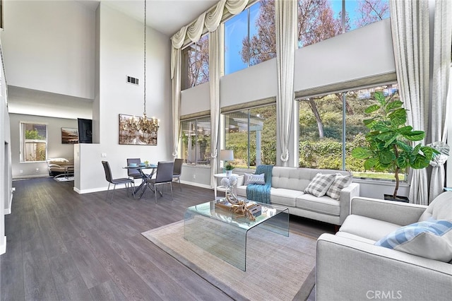 living room with an inviting chandelier, a towering ceiling, and dark wood-type flooring