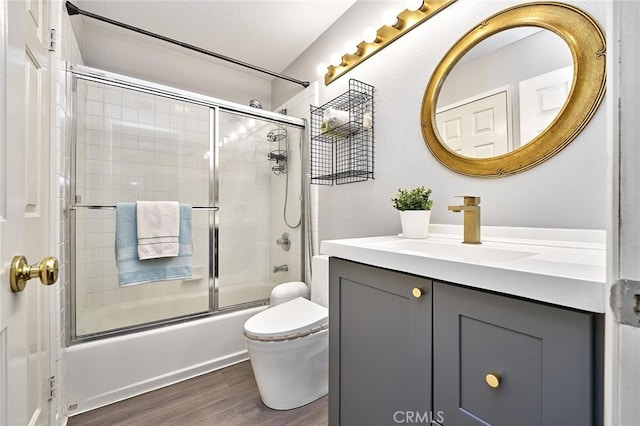 full bathroom featuring a textured ceiling, hardwood / wood-style floors, enclosed tub / shower combo, vanity, and toilet