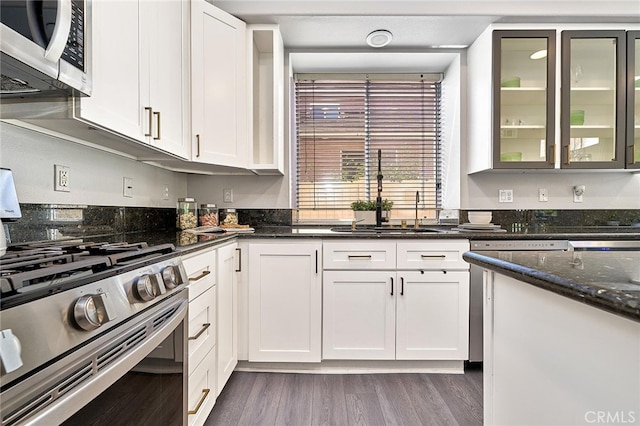 kitchen with appliances with stainless steel finishes, dark stone countertops, white cabinetry, dark hardwood / wood-style floors, and sink