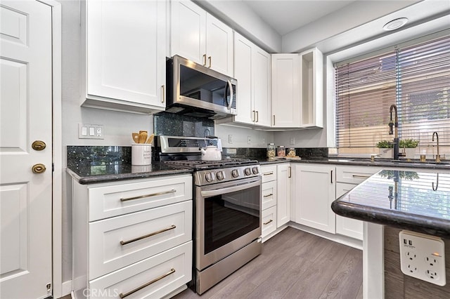 kitchen featuring sink, white cabinetry, stainless steel appliances, hardwood / wood-style floors, and dark stone countertops