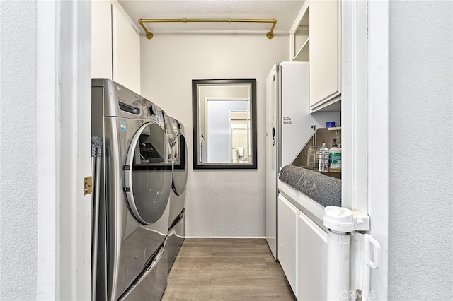 clothes washing area featuring cabinets, a textured ceiling, hardwood / wood-style flooring, and washer and dryer