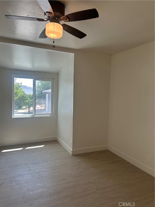 empty room with ceiling fan, baseboards, and wood finished floors