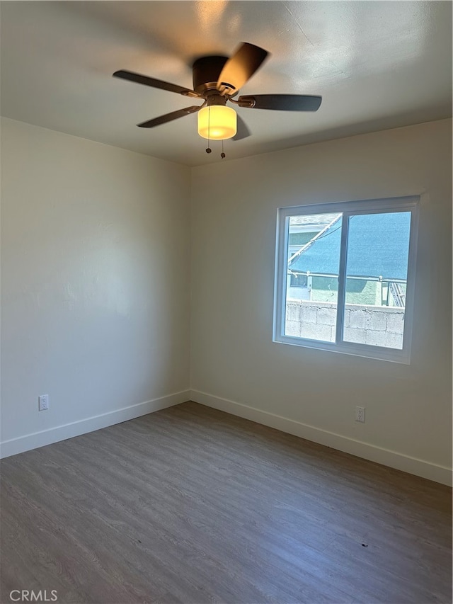 unfurnished room with ceiling fan, baseboards, and dark wood-type flooring