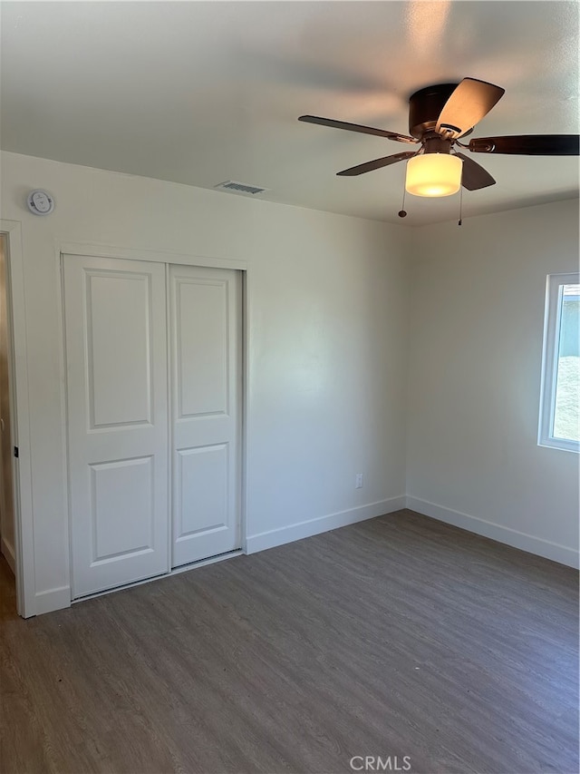 unfurnished bedroom featuring ceiling fan, visible vents, baseboards, a closet, and dark wood finished floors