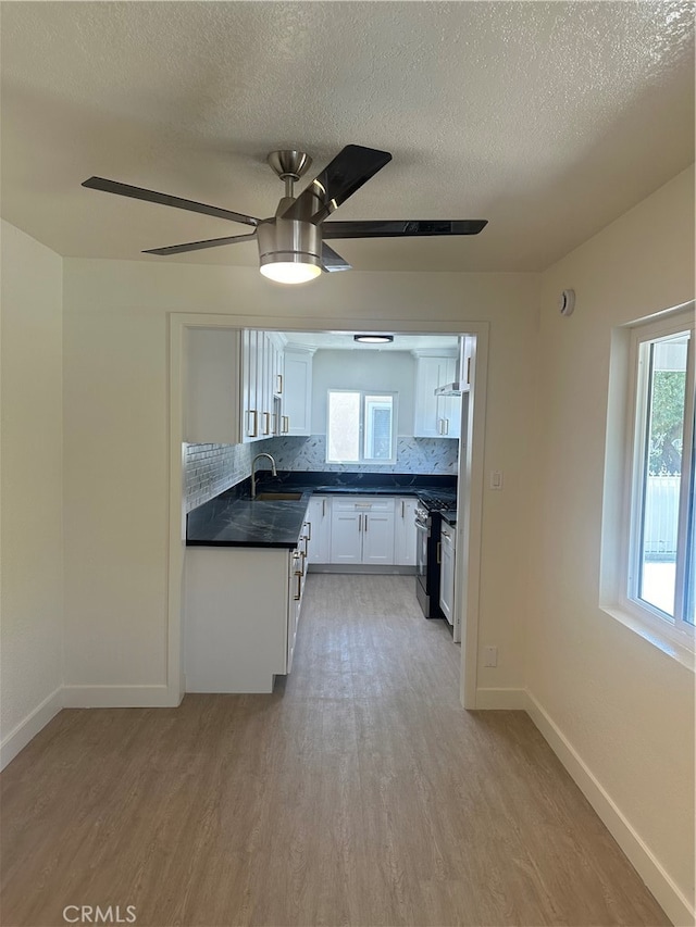 kitchen featuring dark countertops, stainless steel gas range, light wood-style flooring, and backsplash