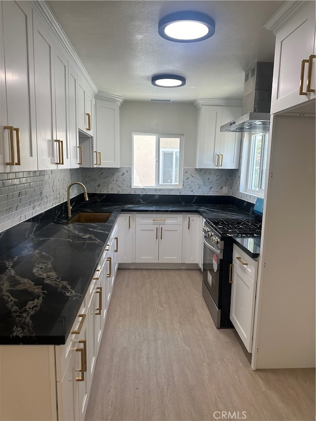 kitchen with a sink, white cabinetry, light wood-type flooring, stainless steel gas stove, and wall chimney exhaust hood