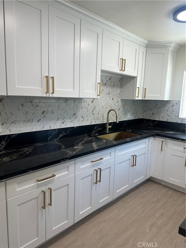 kitchen featuring tasteful backsplash, white cabinets, dark stone countertops, light wood-style floors, and a sink