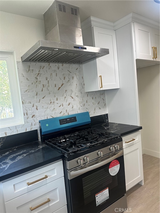 kitchen featuring white cabinetry, stainless steel gas range, backsplash, wall chimney exhaust hood, and dark countertops