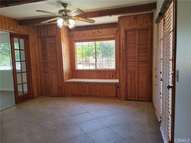 tiled spare room with beam ceiling, wooden walls, french doors, and ceiling fan