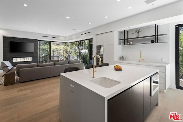 kitchen with a center island with sink, light hardwood / wood-style floors, white cabinets, and sink