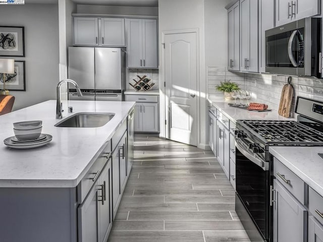 kitchen featuring gray cabinetry, sink, light hardwood / wood-style flooring, light stone counters, and stainless steel appliances