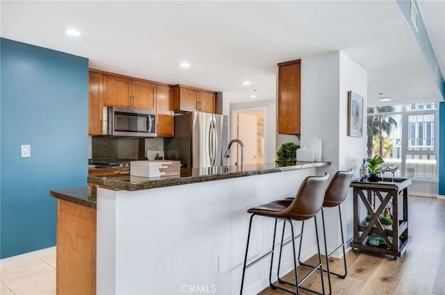 kitchen with dark stone counters, light hardwood / wood-style floors, tasteful backsplash, kitchen peninsula, and appliances with stainless steel finishes