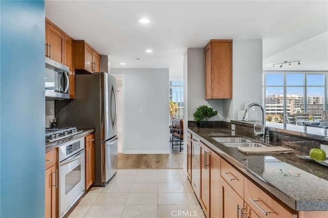 kitchen with sink, rail lighting, light hardwood / wood-style flooring, appliances with stainless steel finishes, and dark stone countertops