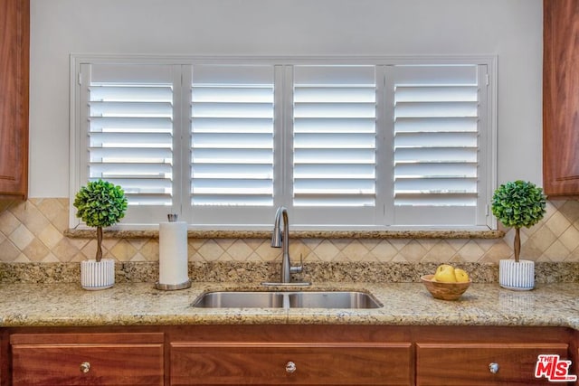 details with backsplash, light stone countertops, and sink