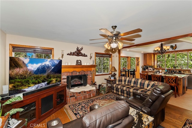 living room with a brick fireplace, ceiling fan with notable chandelier, and light hardwood / wood-style flooring