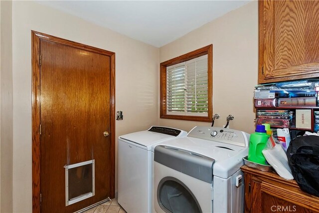 clothes washing area featuring light tile patterned floors, washer and dryer, and cabinets