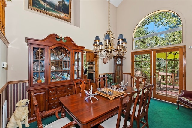 dining area featuring french doors, dark colored carpet, a chandelier, and a high ceiling