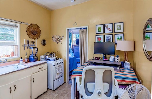 interior space featuring white range with gas stovetop, light tile patterned flooring, white cabinetry, and sink