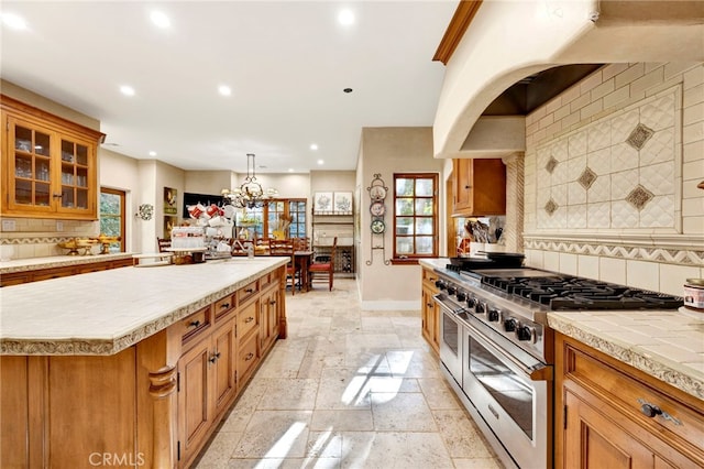 kitchen featuring a center island, tasteful backsplash, a notable chandelier, pendant lighting, and high end range