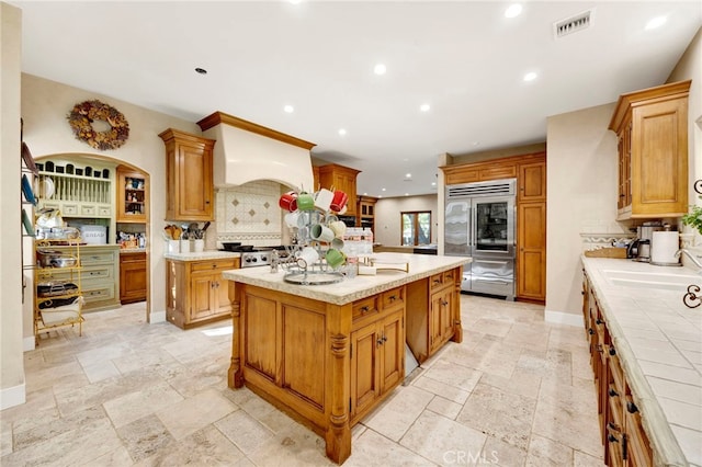 kitchen featuring sink, tasteful backsplash, built in fridge, premium range hood, and a kitchen island