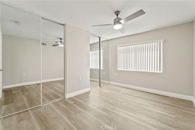 unfurnished bedroom featuring multiple closets, visible vents, light wood-style floors, ceiling fan, and baseboards