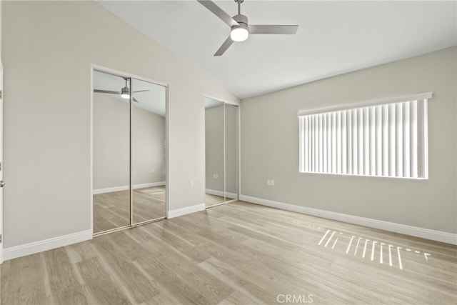 unfurnished bedroom with baseboards, a ceiling fan, vaulted ceiling, light wood-style floors, and two closets